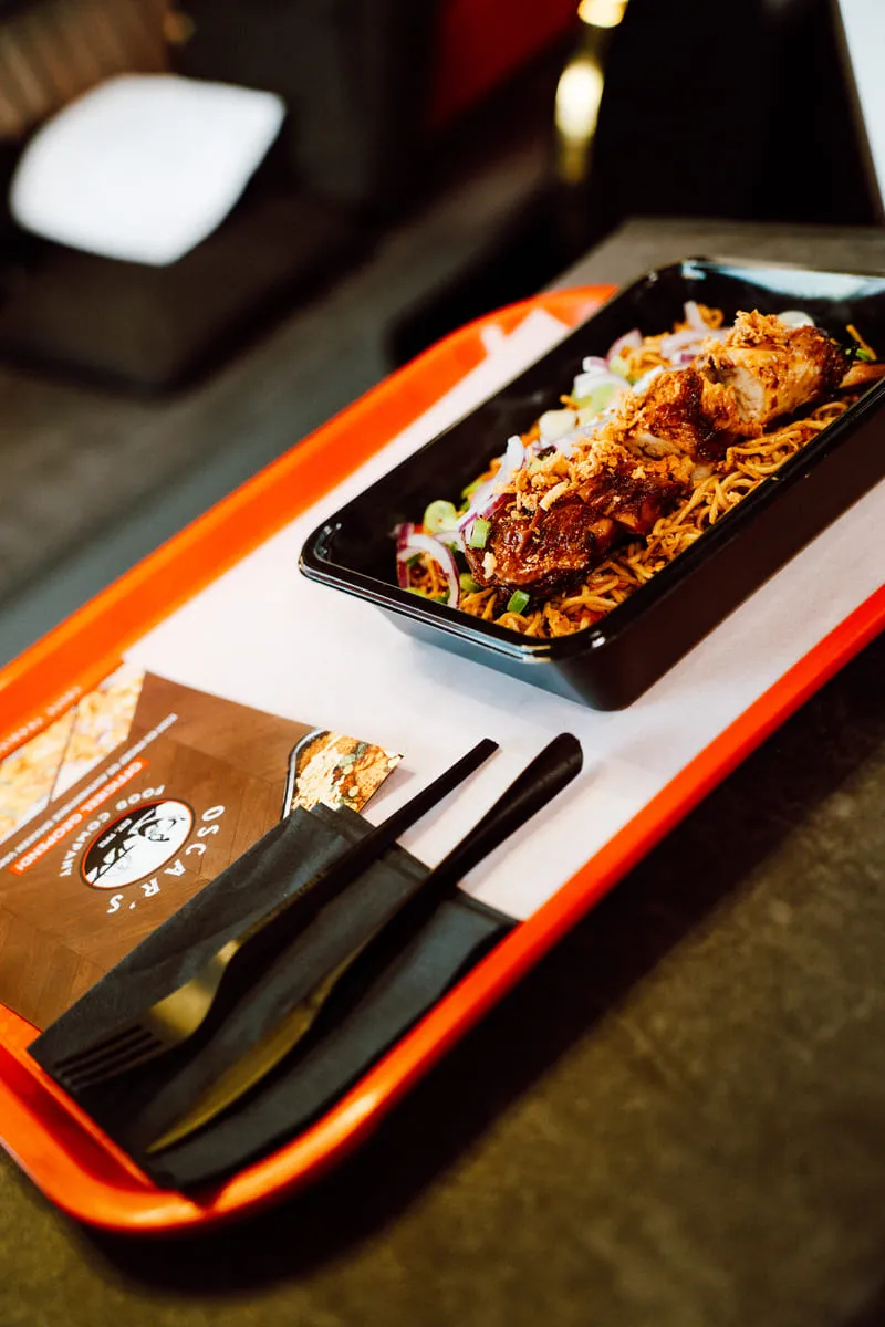 Bami met gegrilde kip en lente-ui op een rood dienblad van Oscar's, met de menukaart ernaast.
