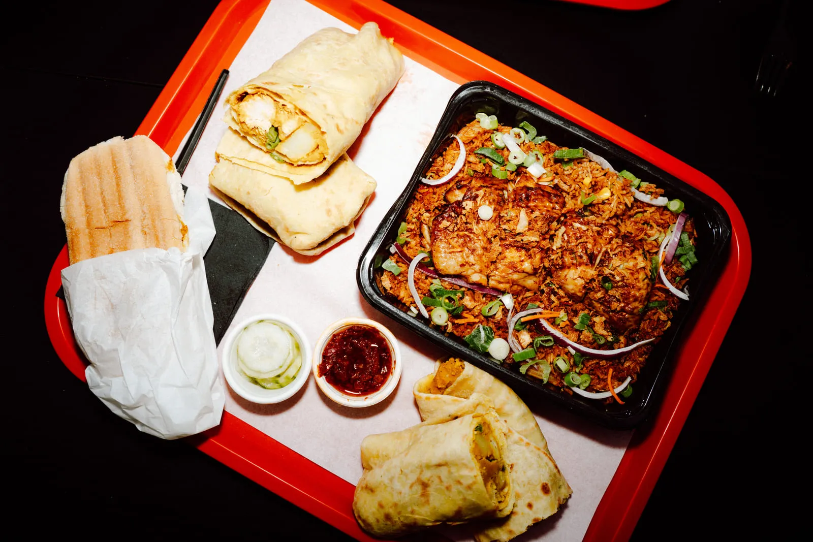 Een vol dienblad met roti, nasi en een Surinaams broodje, van bovenaf op een zwarte tafel.